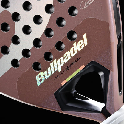Close-up of the Bullpadel Wonder 2026 Padel Racket - Rose Gold, a professional Bullpadel racket with Hyper Core technology. Its textured rose gold surface, black holes, shiny logo text, and detailed handle base stand out.