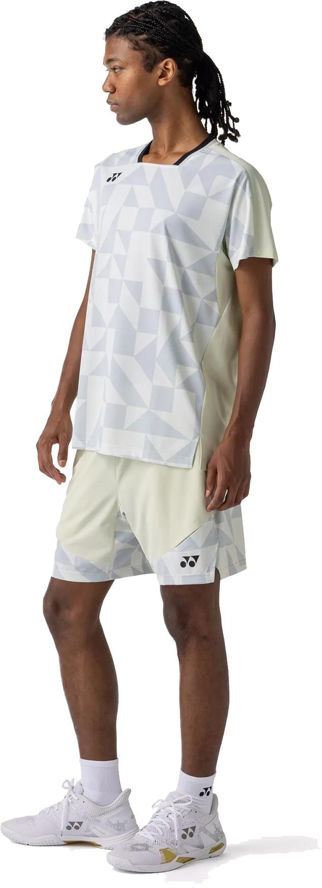 A person stands facing left against a white background, wearing light-colored geometric sports shirt and Yonex 15240YX Knit Mens Padel Shorts - Champagne, paired with white socks and athletic shoes.