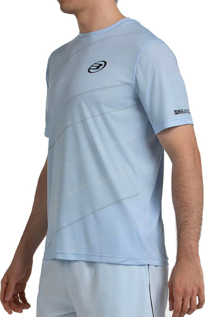 A man wears the Bullpadel Casinas Men's Padel T-Shirt in Glacier Blue, featuring subtle logos on the chest and sleeve. Ideal for performance padel, its Quickerdry technology keeps you comfortable on court.