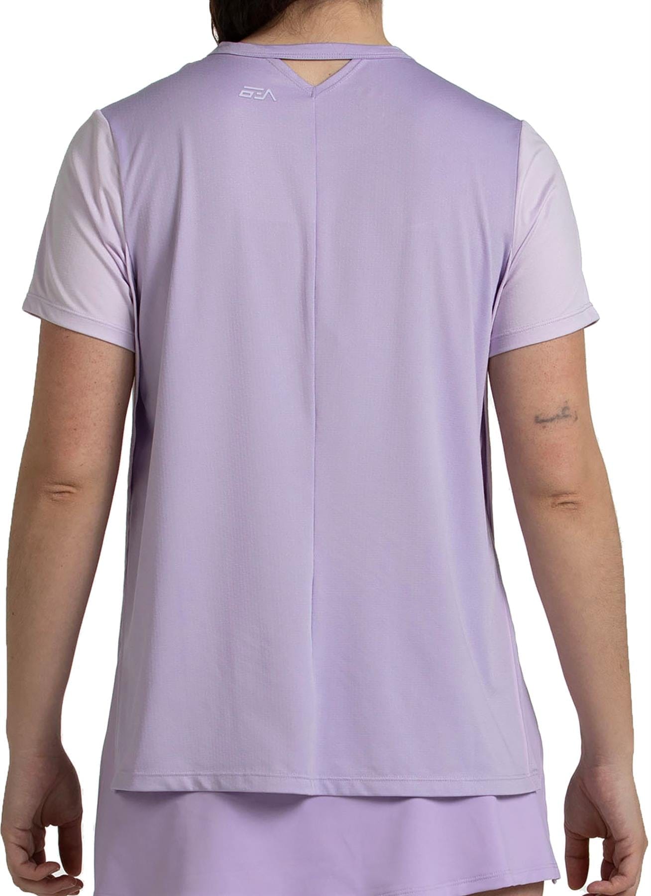A person is shown from the back wearing a Bullpadel Picase Women's Padel T-Shirt in pastel lilac, featuring a small white logo near the neckline, a collar cutout, and moisture-wicking fabric for comfort.