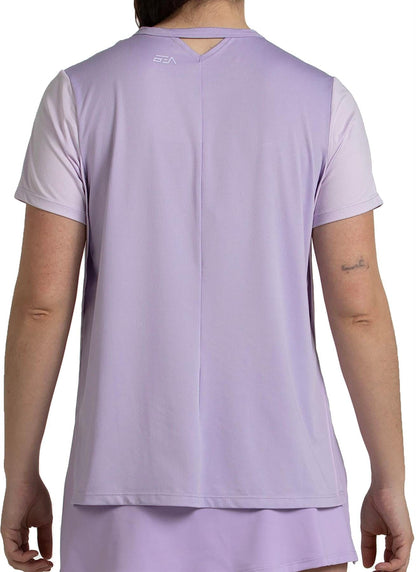 A person is shown from the back wearing a Bullpadel Picase Women's Padel T-Shirt in pastel lilac, featuring a small white logo near the neckline, a collar cutout, and moisture-wicking fabric for comfort.