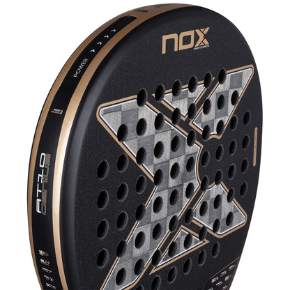 Close-up of NOX AT10 Genius 18K Alum By Agustín Tapia 2026 Padel Racket in black and gold, featuring a prominent "X," circular holes, Dual Spin surface, and "POWER" with "AT10 Genius" branding on the side.