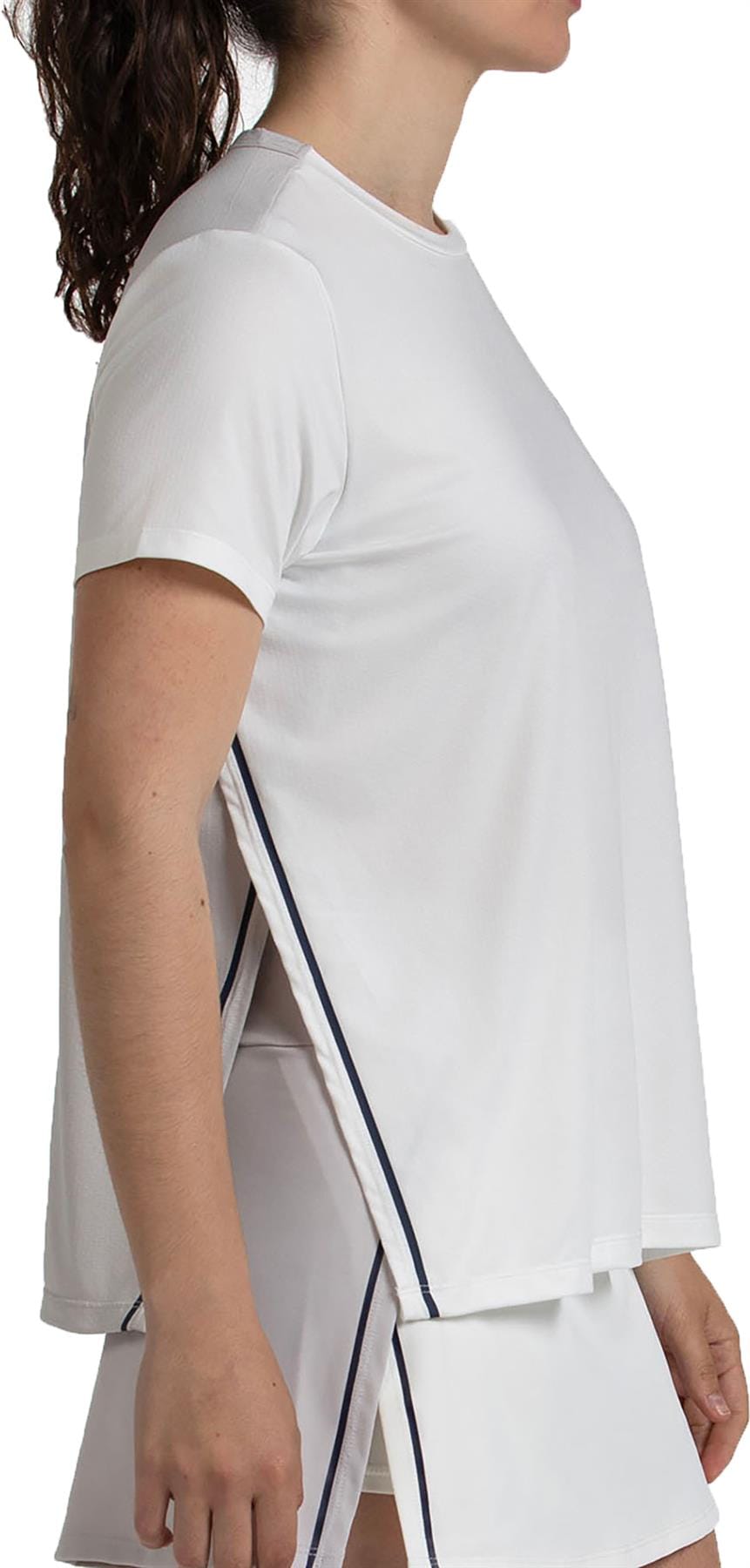 A woman in profile wears a loose-fitting Bullpadel Picase Women's Padel T-Shirt in Bone, paired with matching white shorts with navy trim, set against a plain background.