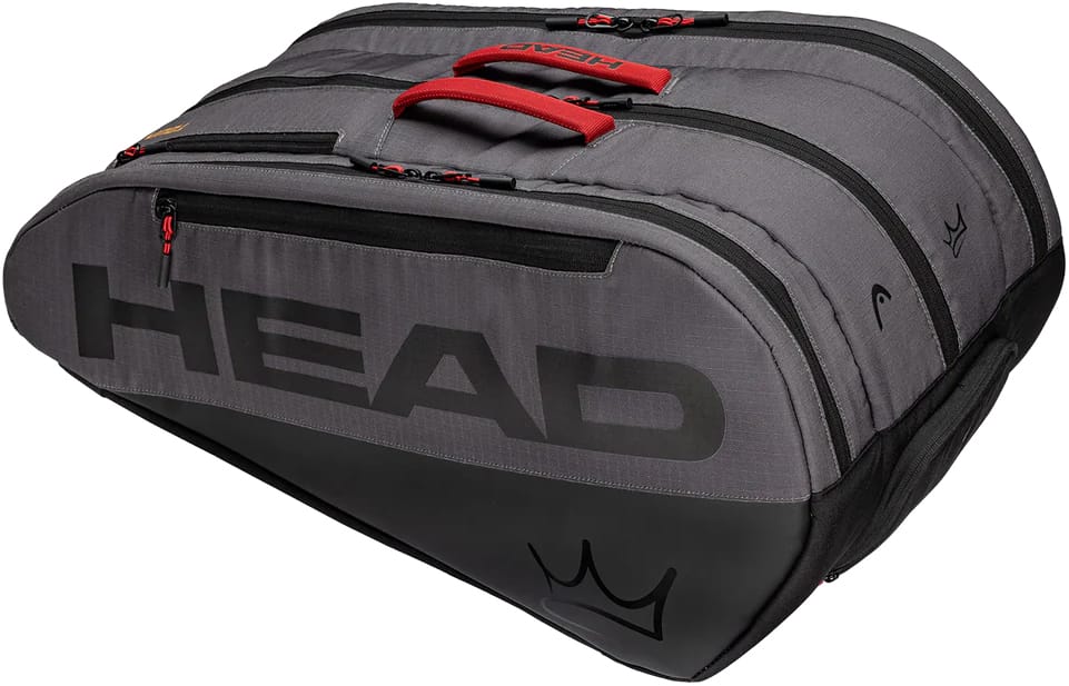 The HEAD Coello Tour Padel Racket Bag L - Dark Grey is a large gray and black bag with striking red handles and zippers, designed with multiple compartments and the signature crown logo on the bottom corner. As part of the exclusive Arturo Coello collection by HEAD, this versatile padel racket bag blends style and functionality, making it ideal for dedicated players.