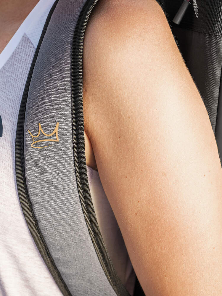 Close-up of a person’s shoulder wearing a sleeveless shirt and carrying the HEAD Coello Tour Padel Racket Bag L in Dark Grey, featuring a small gold crown logo on the strap that reflects the signature style of HEAD’s exclusive Arturo Coello collection.