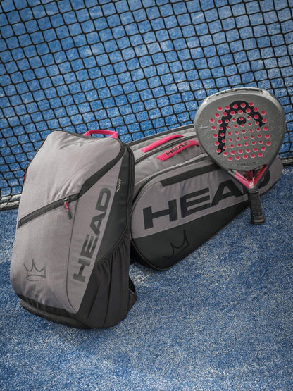 Two dark grey HEAD Coello Tour Padel Racket Bag L bags from HEAD sit on a blue tennis court beside a net. A black and red padel racket rests on top of one of the bags.