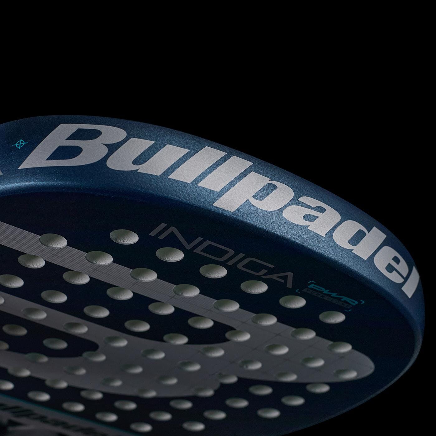 Close-up of the Bullpadel Indiga Pwr 2026 Padel Racket's perforated blue edge, showing "Bullpadel" and "INDIGA" branding against a black background.