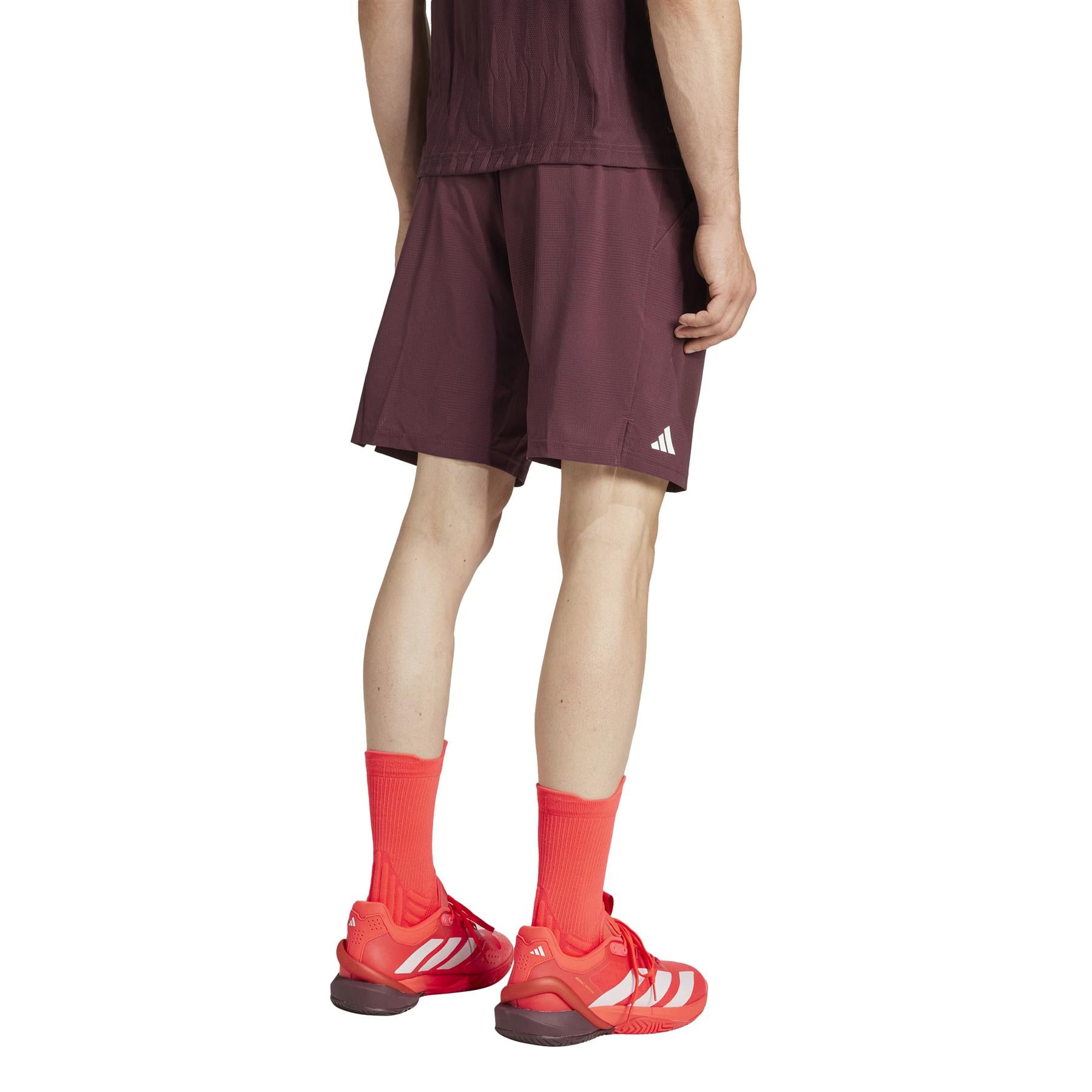 A person in ruby ADIDAS Ergo Men's Padel Shorts, made from recycled materials, is shown from behind. They're wearing bright red socks and sports shoes.