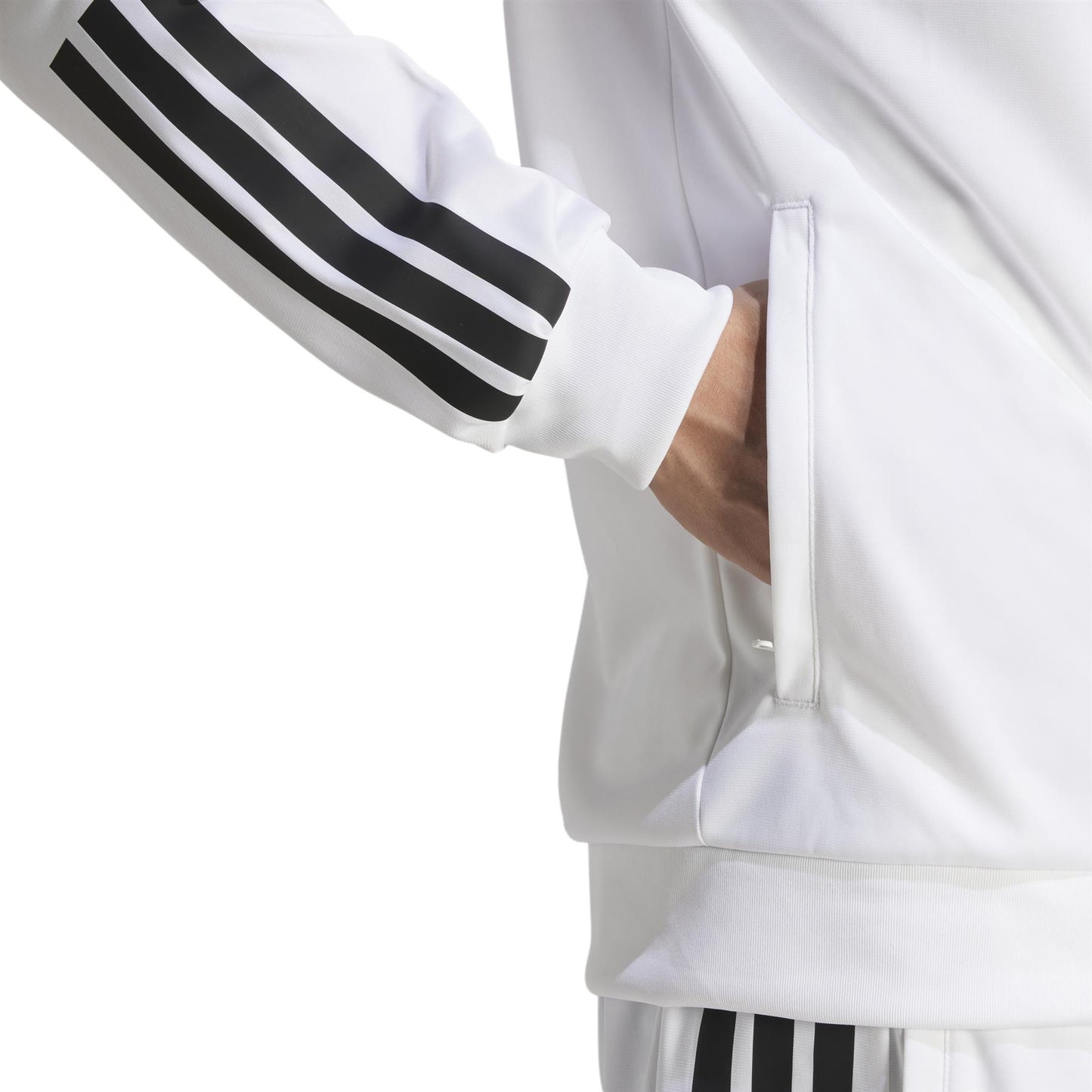 A person is wearing the adidas Men's 3 Stripe Knit Padel Jacket in white, featuring three black stripes on the sleeves and pants. Their right hand is in the jacket's side pocket against a plain white background.