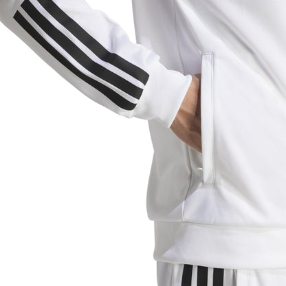 A person is wearing the adidas Men's 3 Stripe Knit Padel Jacket in white, featuring three black stripes on the sleeves and pants. Their right hand is in the jacket's side pocket against a plain white background.