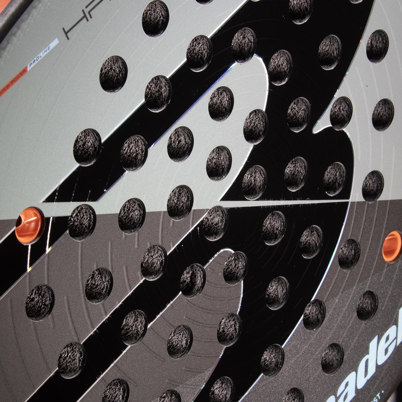 Close-up of the Bullpadel HACK 04 Comfort 2026 Padel Racket in grey, featuring textured circular holes and a bold “B” logo, designed by Bullpadel to deliver dynamic power on the court.