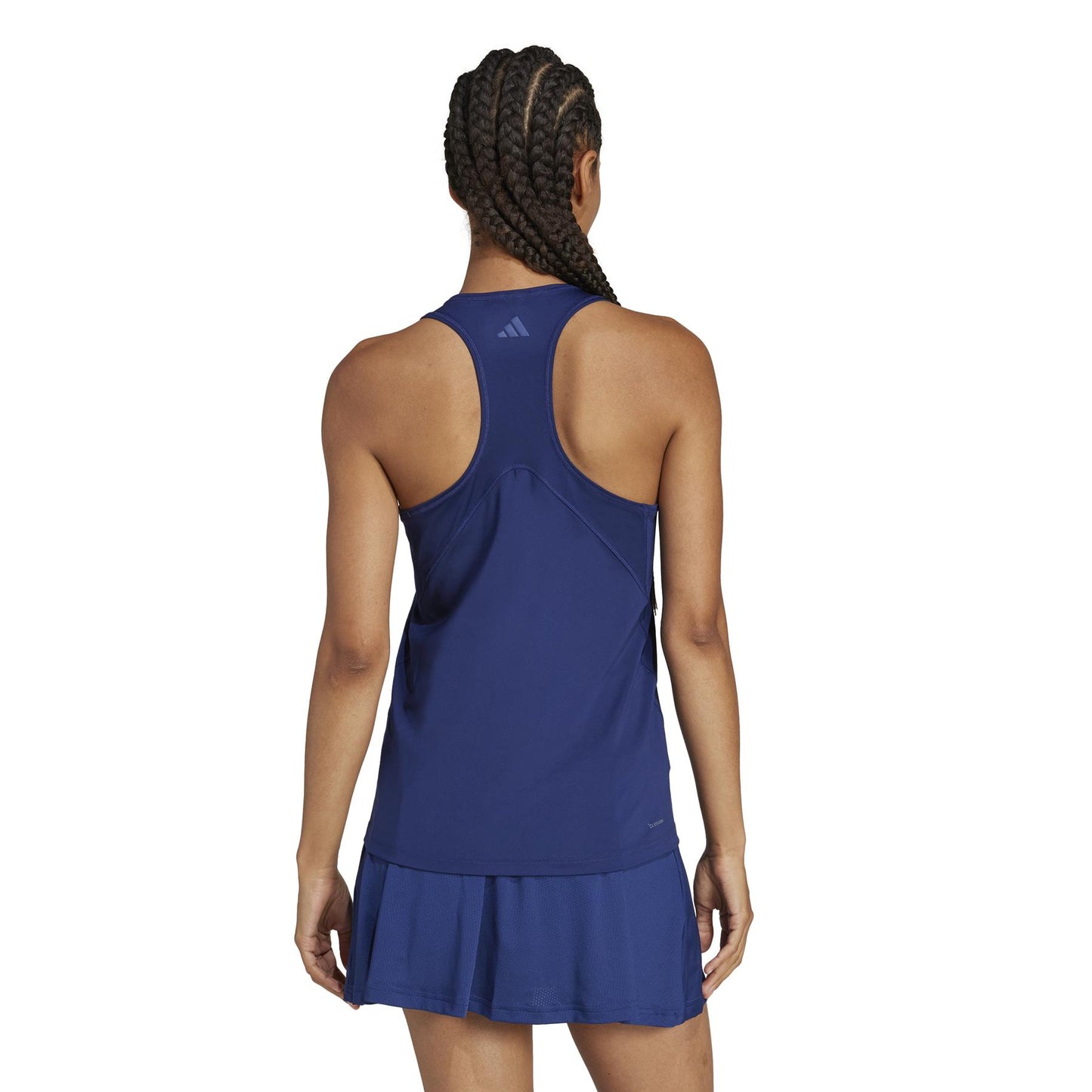 A person with braided hair faces away, wearing a navy adidas Women's Club Padel Tank Top and matching skirt made from recycled materials, both featuring Adidas logos. The outfit stands out with its sleek design against a crisp white background.