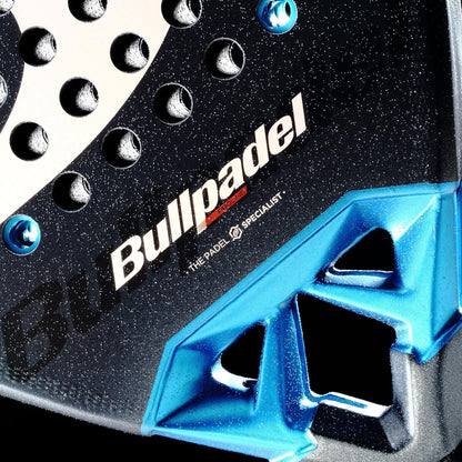 Close-up of the Bullpadel Vertex 05 Comfort 2026 Padel Racket in black and blue, featuring the Bullpadel branding, a textured surface with round holes, and a durable metallic blue Fibrix fibre section with geometric cutouts.