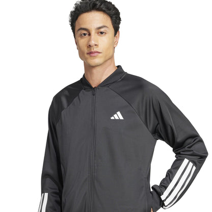 A person wears the black ADIDAS Men's 3 Stripe Knit Padel Jacket, featuring white sleeves and an adidas logo on the chest, with one hand in their pocket.