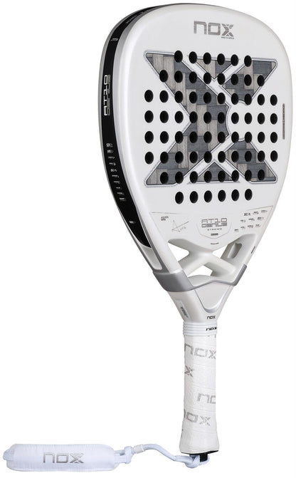 The NOX AT10 Genius Attack 12K Alum Extrem By Agustín Tapia 2026 Padel Racket features a white design, bold black "X" on the face, round holes, a white grip handle, and a wrist strap with the NOX logo for ultimate power on court.