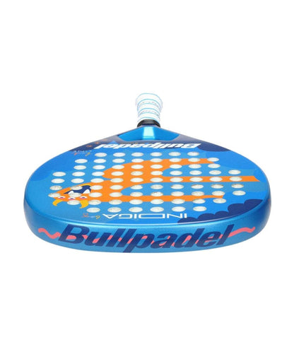The Bullpadel INDIGA Junior Boys 2026 Padel Racket features a blue design with circular face holes, orange and white accents, and Bullpadel branding on the head and handle. Shown from the front to highlight its structure and details.