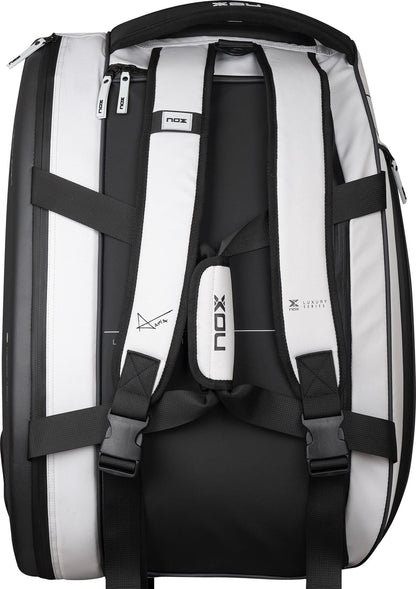 The NOX Luxury Master Series Padel Racket Bag in black and white features padded shoulder straps, black buckles, zipper compartments, and "NOX" branding on the bag and straps. Inspired by Miguel Lamperti, it is shown from the back.