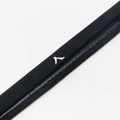 Close-up of a Kanso Headband strap from the Kanso Headband - 3 Pack - Black, showcasing a small white triangle logo. The strap's soft, velvety texture is accented by a thin glossy line, perfect for keeping hair tidy. It rests on a plain, light-colored background.