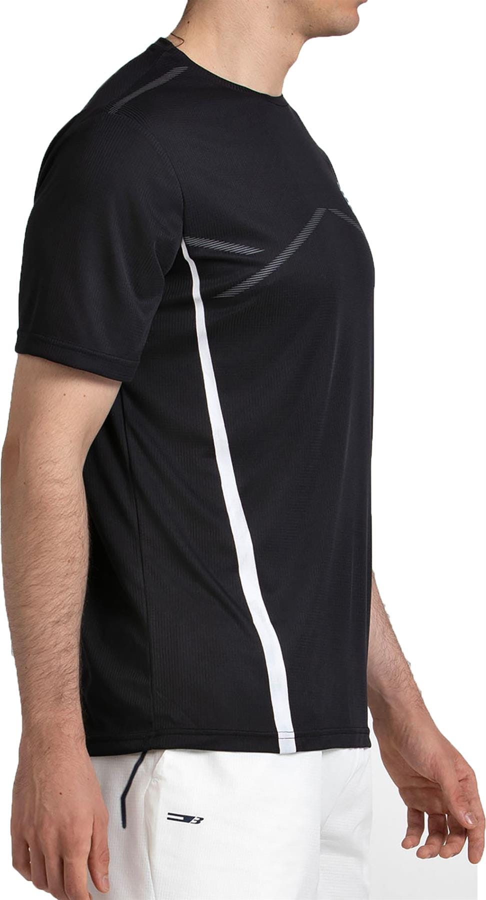 A man stands in side profile wearing the Bullpadel Cabore Mens Padel T-Shirt in black with white side stripes and white shorts. Made by Bullpadel, this quick-drying shirt is ideal for active wear.