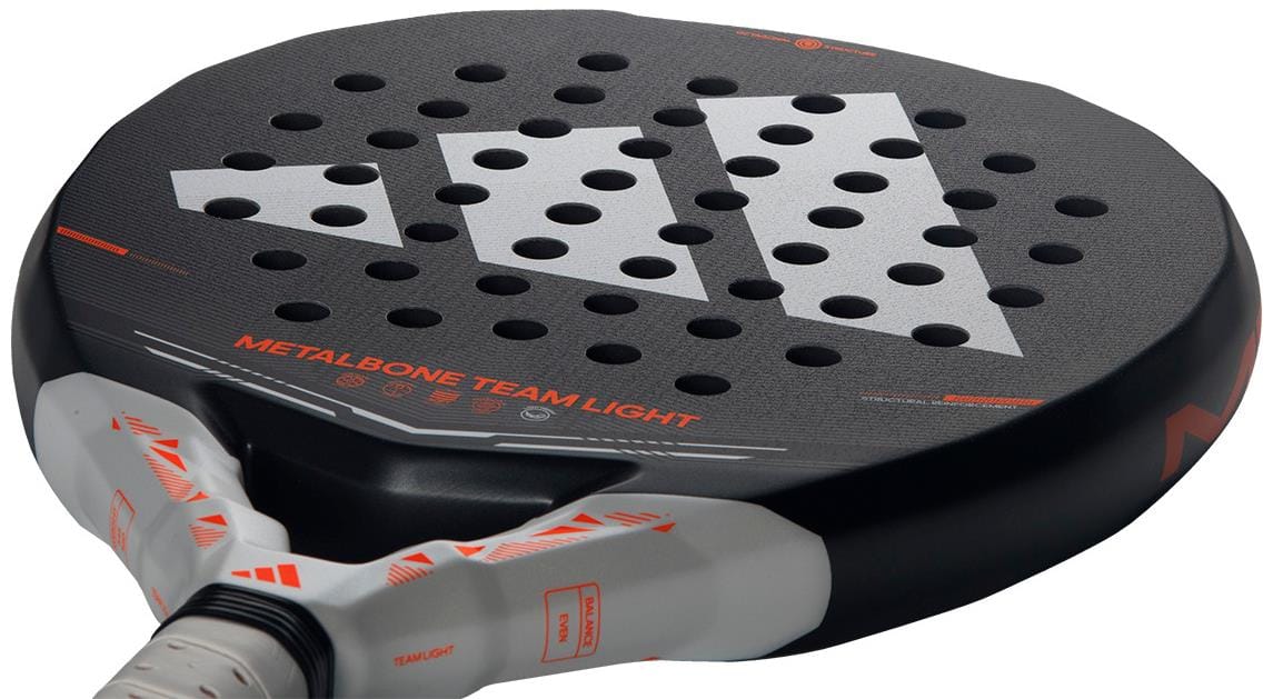 A close-up of the adidas Metalbone Team Light 2026 Padel Racket - Black for advanced players, showing a large white adidas logo, many circular holes, and "METALBONE TEAM LIGHT" printed in orange on the surface.