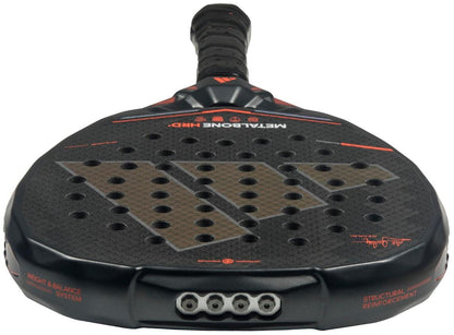 Close-up of the adidas Metalbone HRD+ by Ale Galán 2026 Padel Racket in black and red, showcasing its textured, hole-punched surface, black grip tape handle, and branded technical details on the frame.