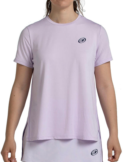 A person wears the Bullpadel Picase Women's Padel T-Shirt in Pastel Lilac, featuring a small dark logo on the left chest and a matching skirt, both from Bullpadel performance apparel, shown front-facing with their head partially out of frame.