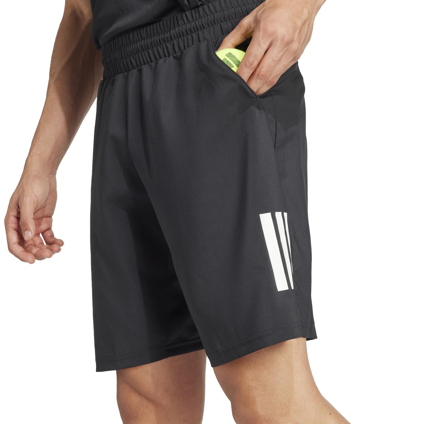 A person in adidas Men's 3 Stripe Padel Shorts - Black, with a white logo on the left leg and featuring an elastic waistband, places something into a pocket while their upper body is partially visible.