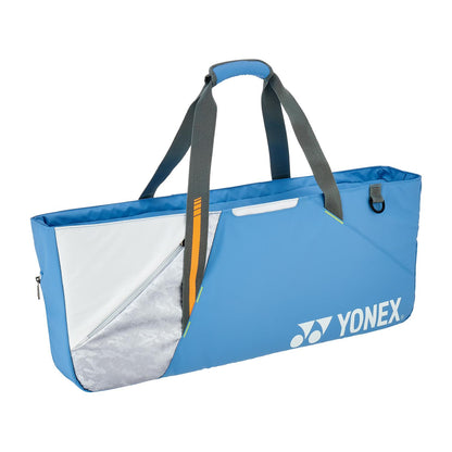 The Yonex 52531EX Club Tournament Padel Bag in grayish blue features gray straps, a white and silver geometric design on one side, a small attachment loop, and a racket divider. The Yonex logo is printed in white on the bottom right corner.