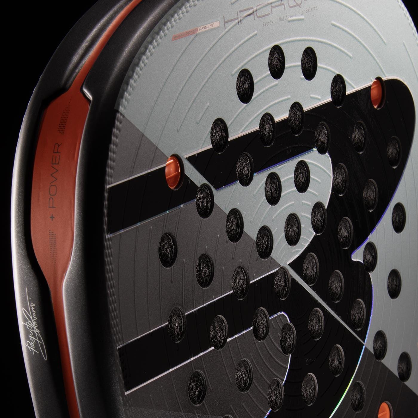 Close-up of the Bullpadel HACK 04 Comfort 2026 Padel Racket in grey, featuring circular perforations, orange edge details, and prominent Bullpadel branding on the frame for dynamic power.