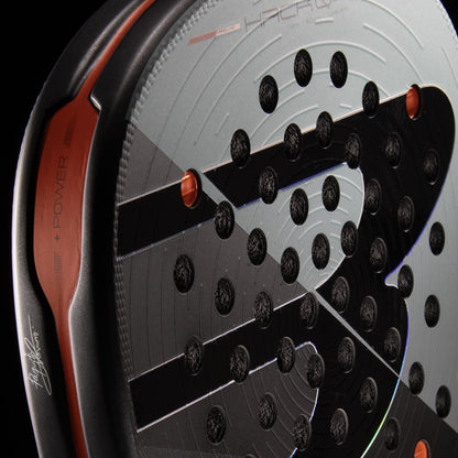 Close-up of the Bullpadel HACK 04 Comfort 2026 Padel Racket in grey, featuring circular perforations, orange edge details, and prominent Bullpadel branding on the frame for dynamic power.