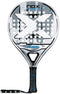 The NOX X-Hero White Padel Racket features a black, white, and gray design with a large central X, round holes on the head, and a black grip handle with an attached wrist strap.