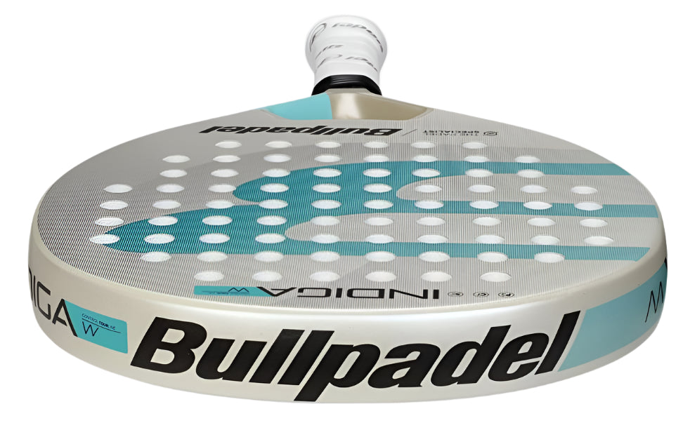 A close-up of the ultralight Bullpadel Indiga W 2025 padel racket with its black brand logo on a beige and turquoise body, and a white grip handle, lying flat.