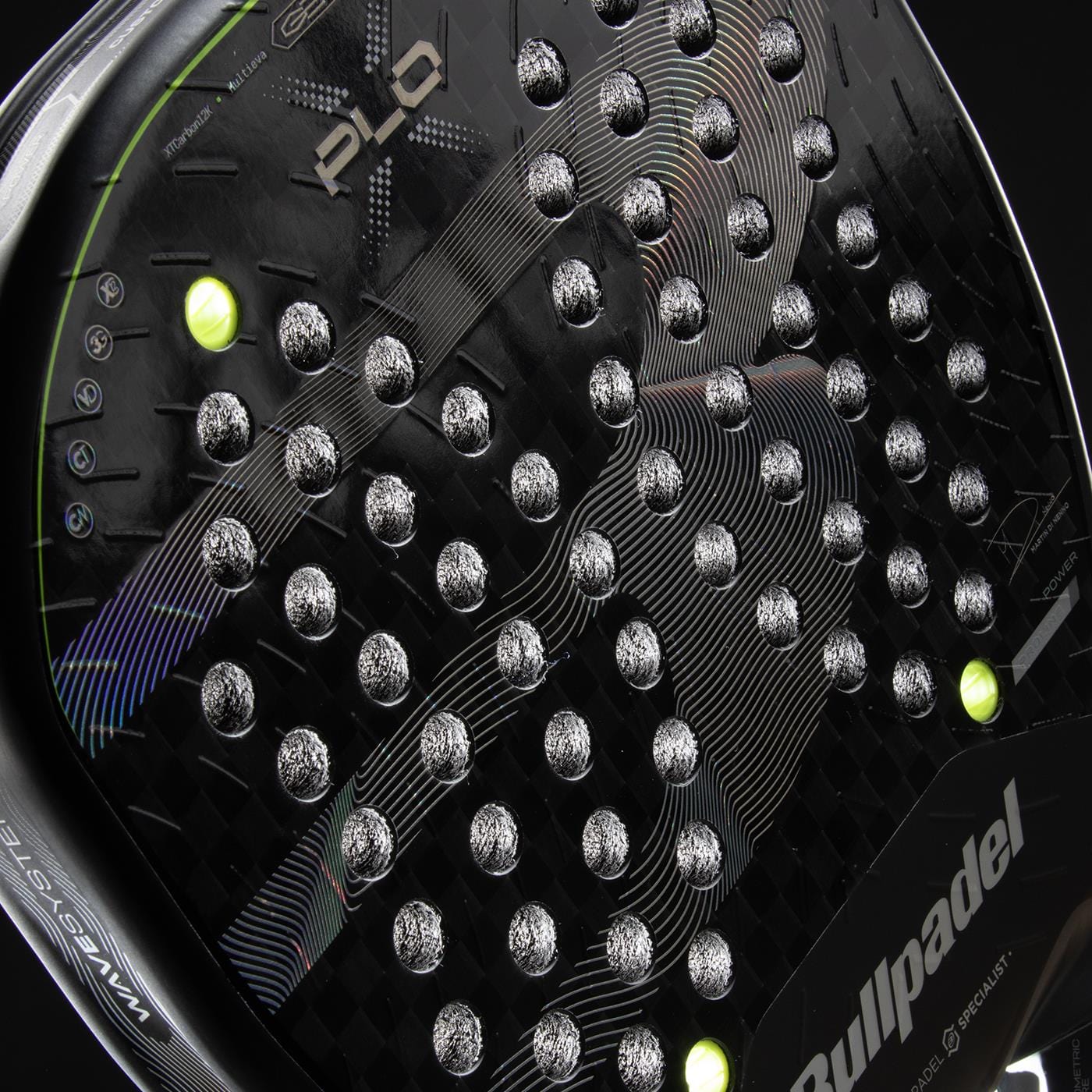 Close-up of the Bullpadel XPLO 2026 Padel Racket - Black, featuring a textured black surface with silver accents and two yellow-green balls partially visible behind this professional Bullpadel racket.