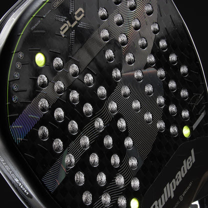 Close-up of the Bullpadel XPLO 2026 Padel Racket - Black, featuring a textured black surface with silver accents and two yellow-green balls partially visible behind this professional Bullpadel racket.