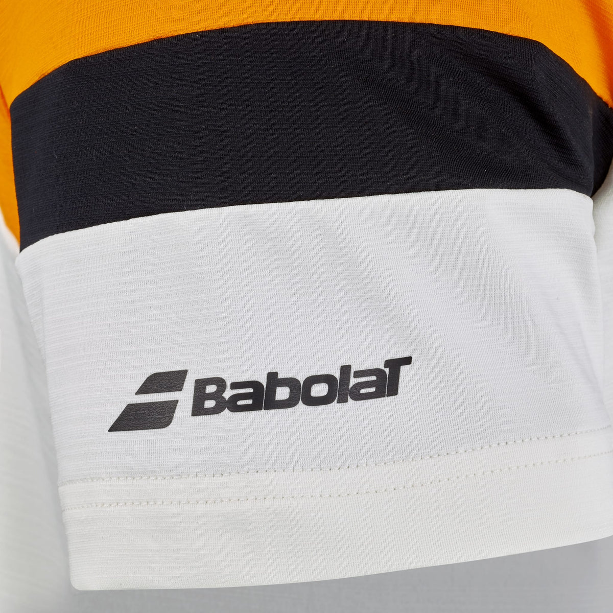 A close-up of the Babolat Crew Neck Men’s Padel T-Shirt in orange and cream, featuring bold color blocks. The cream section displays the Babolat logo in black, showcasing this stylish crew neck tee designed by Babolat for padel players.