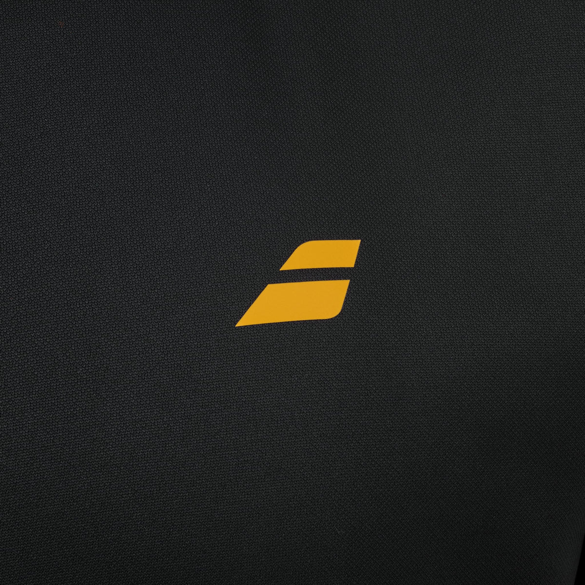 A small, stylized yellow “S” logo is centered on a black textured background—echoing the crisp design details of the Babolat Perf Mens Padel Jacket - Black by Babolat, a lightweight and breathable jacket designed for performance both on and off the court.