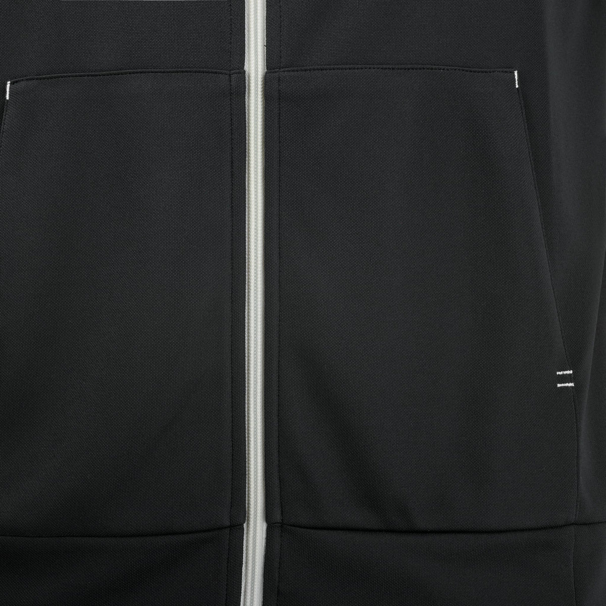 Close-up of the Babolat Perf Men’s Padel Jacket in black, featuring a white zipper and two front pockets with a minimalistic design and subtle stitching details. This lightweight, breathable men’s padel court jacket from Babolat offers optimal comfort and style on the court, making it an excellent choice for players seeking both functionality and a sleek look.