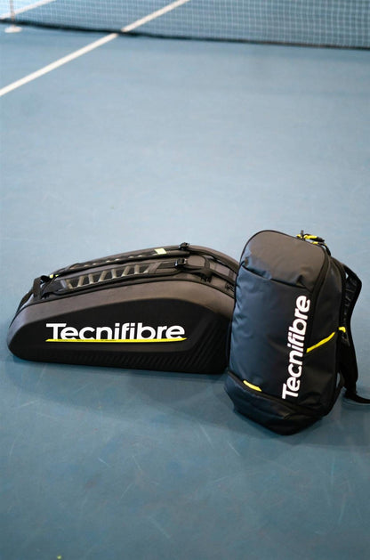 A black Tecnifibre Reform Padel Backpack and a Tecnifibre duffel bag sit on the blue tennis court near the net, both featuring yellow accents, white Tecnifibre logos, and durable EVA material for protection.