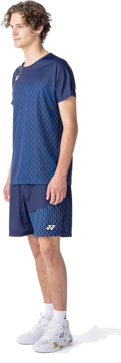 A person wears a Yonex 10713EX Crew Neck Men’s Padel T-Shirt in dark navy with matching shorts, white socks, and white athletic shoes, facing slightly left against a white background.