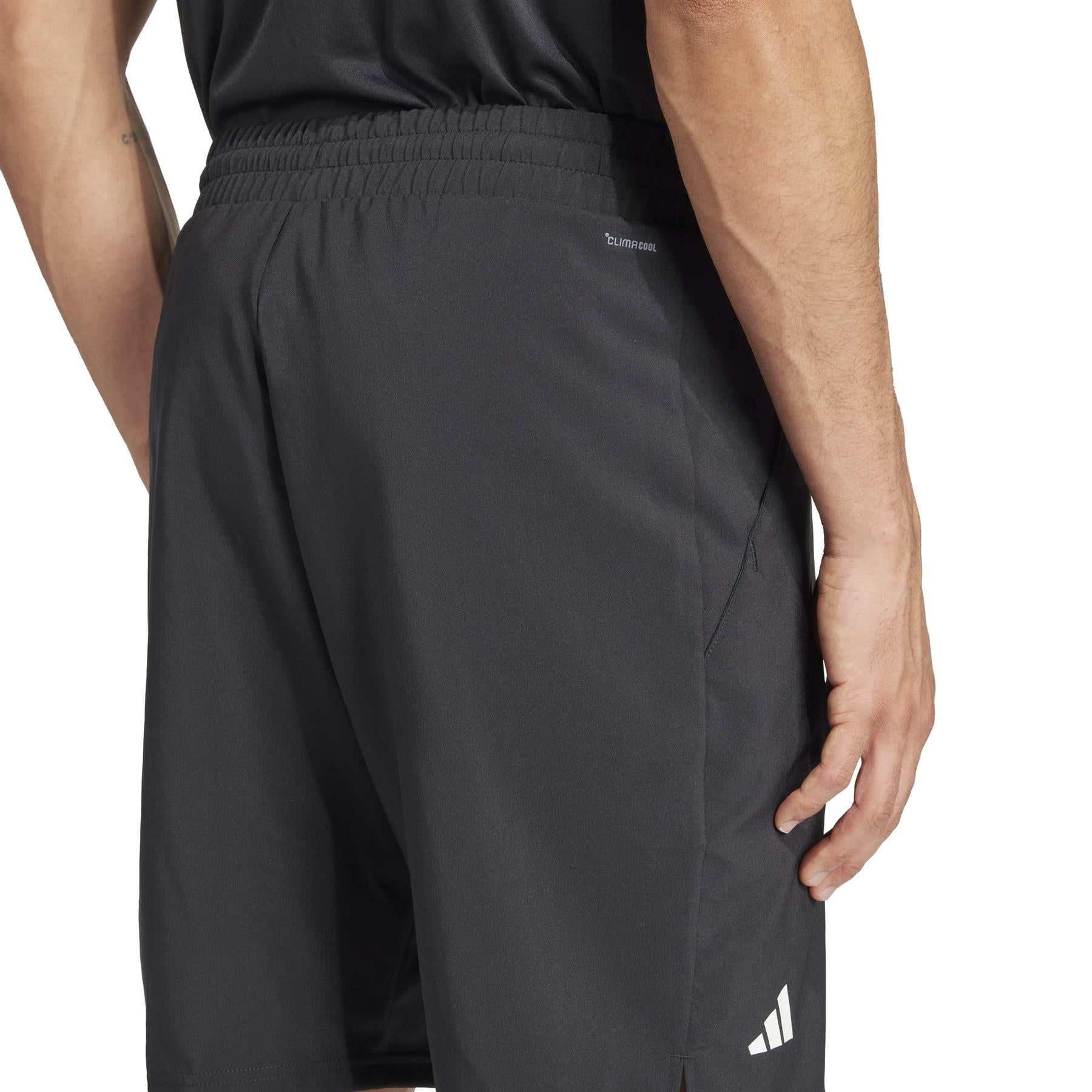 A person is seen from behind wearing black shorts and a shirt. The ADIDAS Mens 3 Stripe Padel Shorts by adidas have a small logo, side pockets, and moisture-wicking fabric. Their right hand is near the pocket.