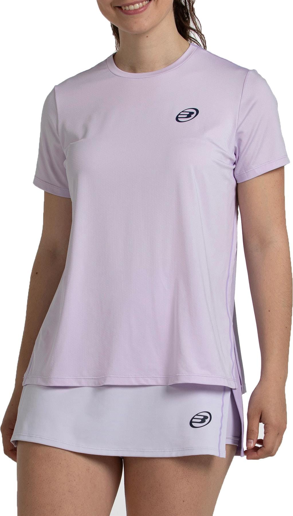 A woman smiles, standing mid-thigh up against a plain background, wearing the Bullpadel Picase Women’s Padel T-Shirt in Pastel Lilac—stylish performance apparel by Bullpadel, ideal for any padel game.