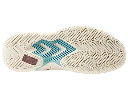 The image shows the sole of the K-Swiss Tura Team Women's Padel Shoes, featuring a beige herringbone pattern for grip with teal and pink accents. Two chevron-like designs and a circular logo are present on one side.