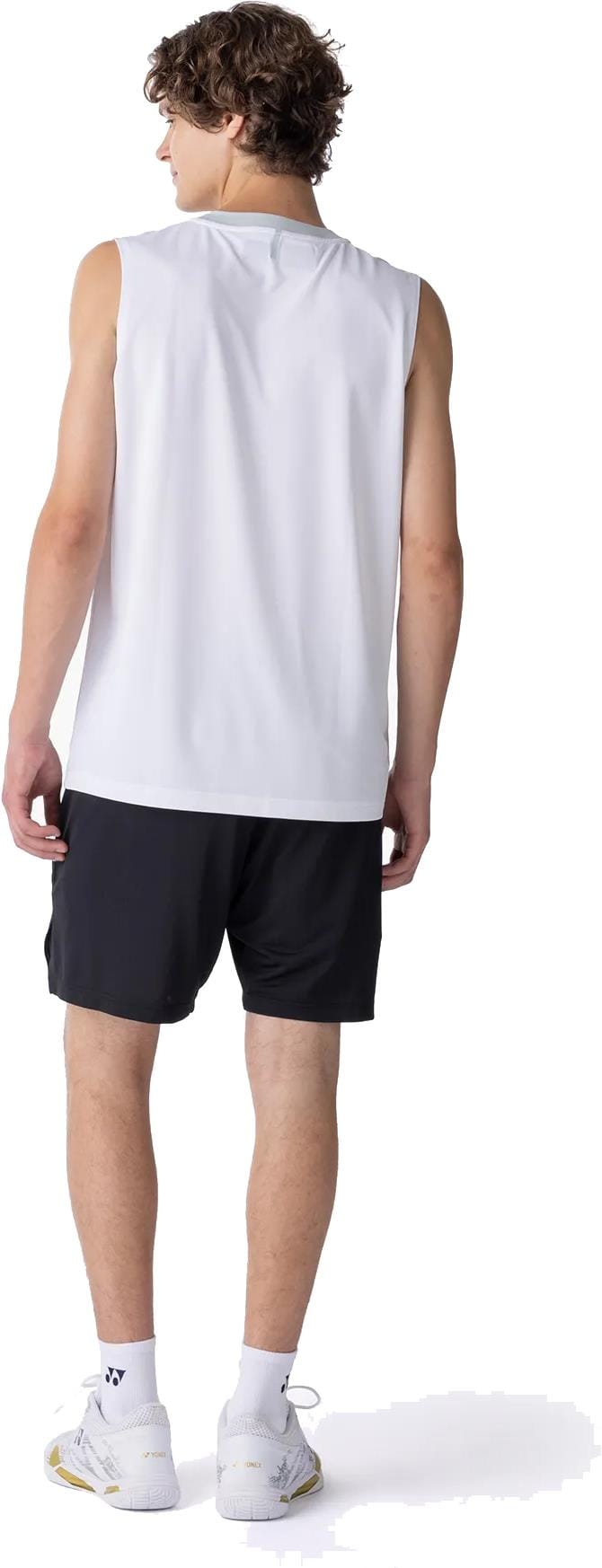 A man with short, curly brown hair faces away, wearing a sleeveless white shirt, Yonex 15239YX Knit Men's Padel Shorts in black, white crew socks, and white athletic shoes against a plain white background.