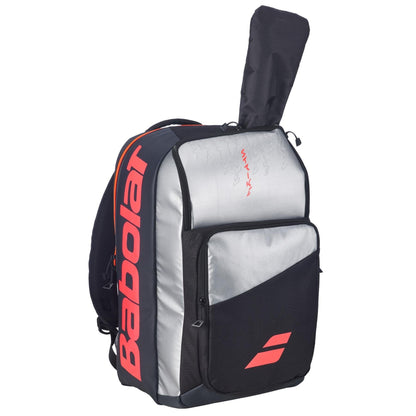 The Babolat Pure Strike Tennis Backpack – Carbon Grey features a large red logo, multiple compartments, and a top sleeve with a tennis racket partially visible.