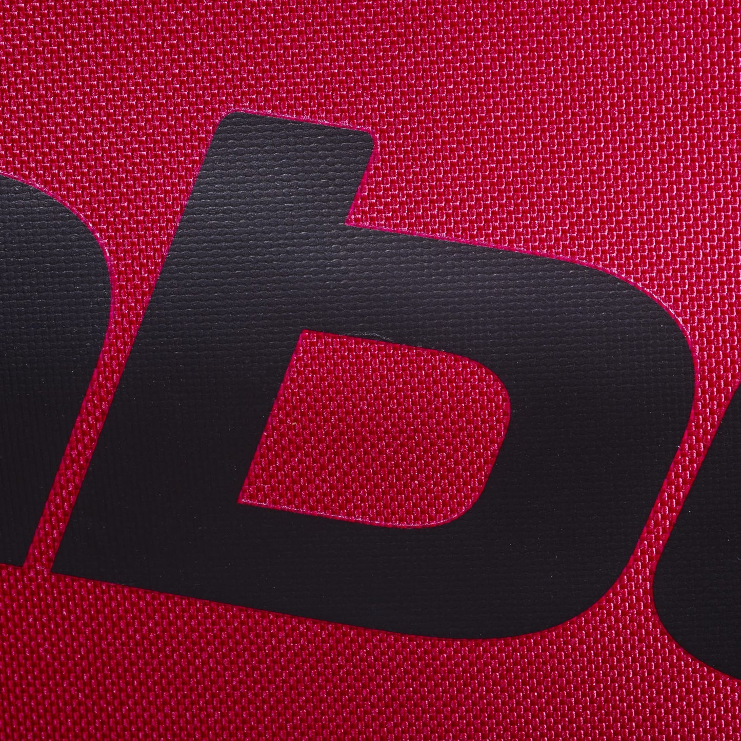 Close-up of a black letter "b" printed on textured burgundy fabric, likely part of the Babolat logo, as seen on the Babolat Court S Padel Racket Bag - Burgundy.