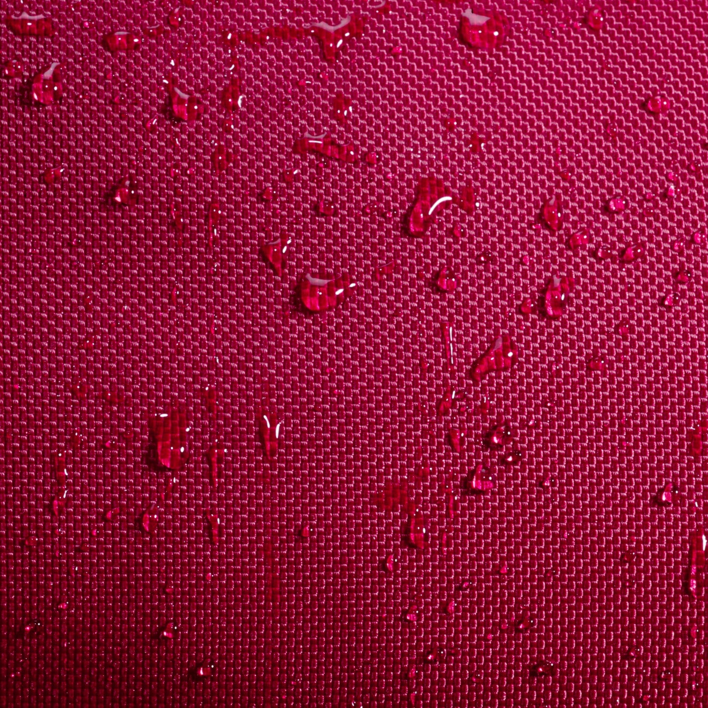 Close-up of water droplets resting on a textured, deep burgundy fabric surface, similar to the durable material featured on the Babolat Court S Padel Racket Bag by Babolat. The grid-like pattern beneath the droplets highlights the exceptional craftsmanship and quality typical of premium padel gear.