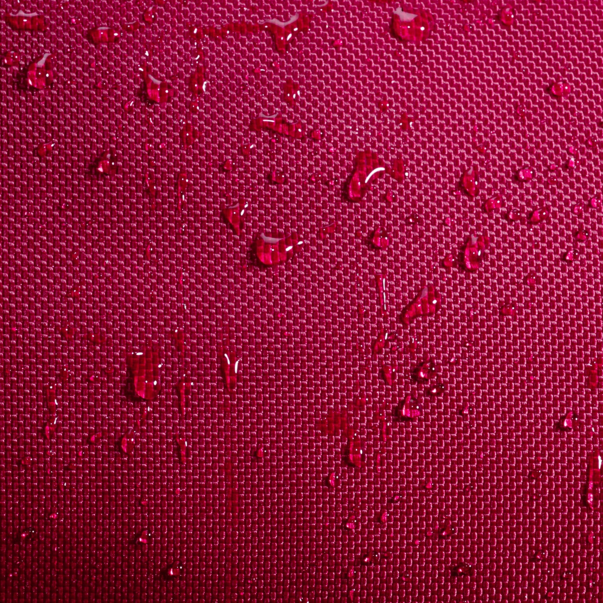 Close-up of water droplets resting on a textured, deep burgundy fabric surface, similar to the durable material featured on the Babolat Court S Padel Racket Bag by Babolat. The grid-like pattern beneath the droplets highlights the exceptional craftsmanship and quality typical of premium padel gear.