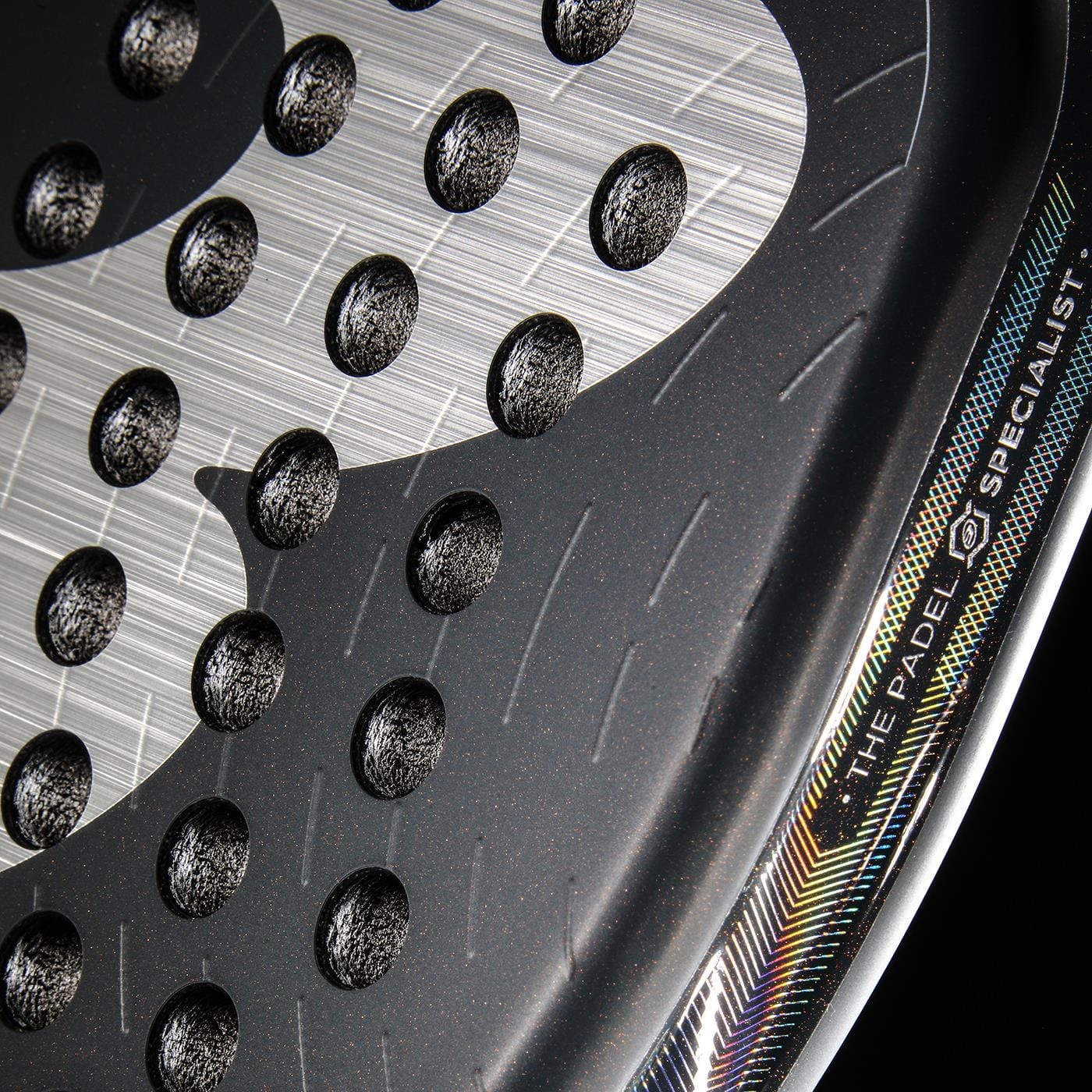Close-up of the Bullpadel XPLO Comfort 2026 Padel Racket - Grey, featuring circular holes, a textured surface, and "THE PADEL SPECIALIST" in a rainbow edge—engineered by Bullpadel for comfort and control on the court.