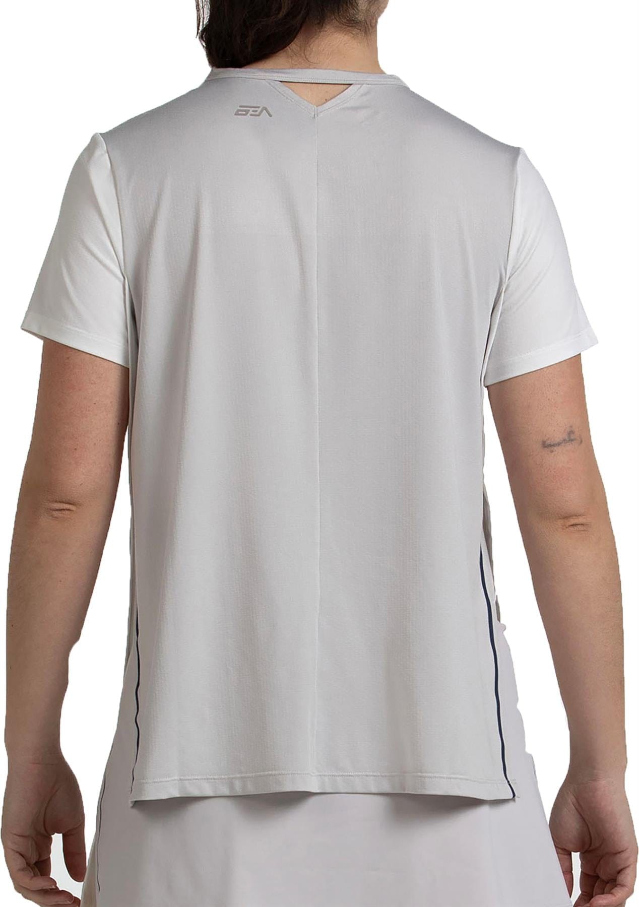 A woman is shown from the back wearing a Bullpadel Picase Women’s Padel T-Shirt in Bone, featuring short sleeves, moisture-wicking fabric, a small Bullpadel logo near the neck, and a keyhole detail below the collar.