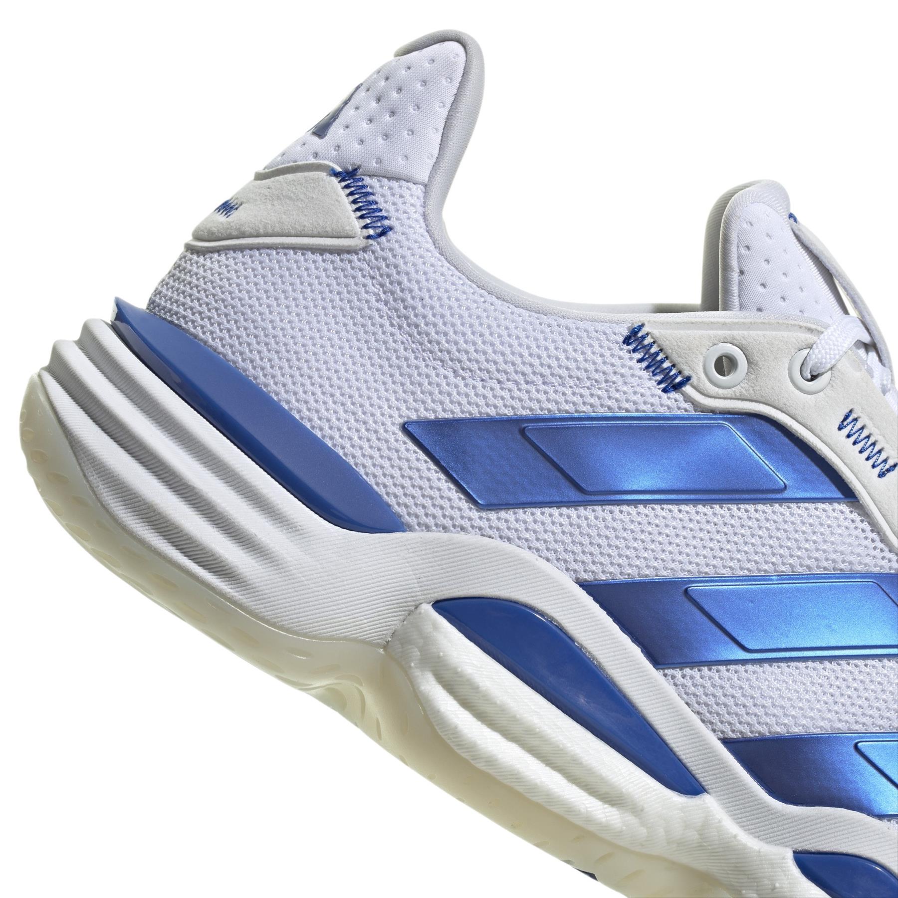 Close-up of an adidas Stabil 16 Men's Padel Shoe in white and blue with textured mesh and metallic blue stripes. It features a thick white BOOST midsole with blue accents and a cushioned heel.